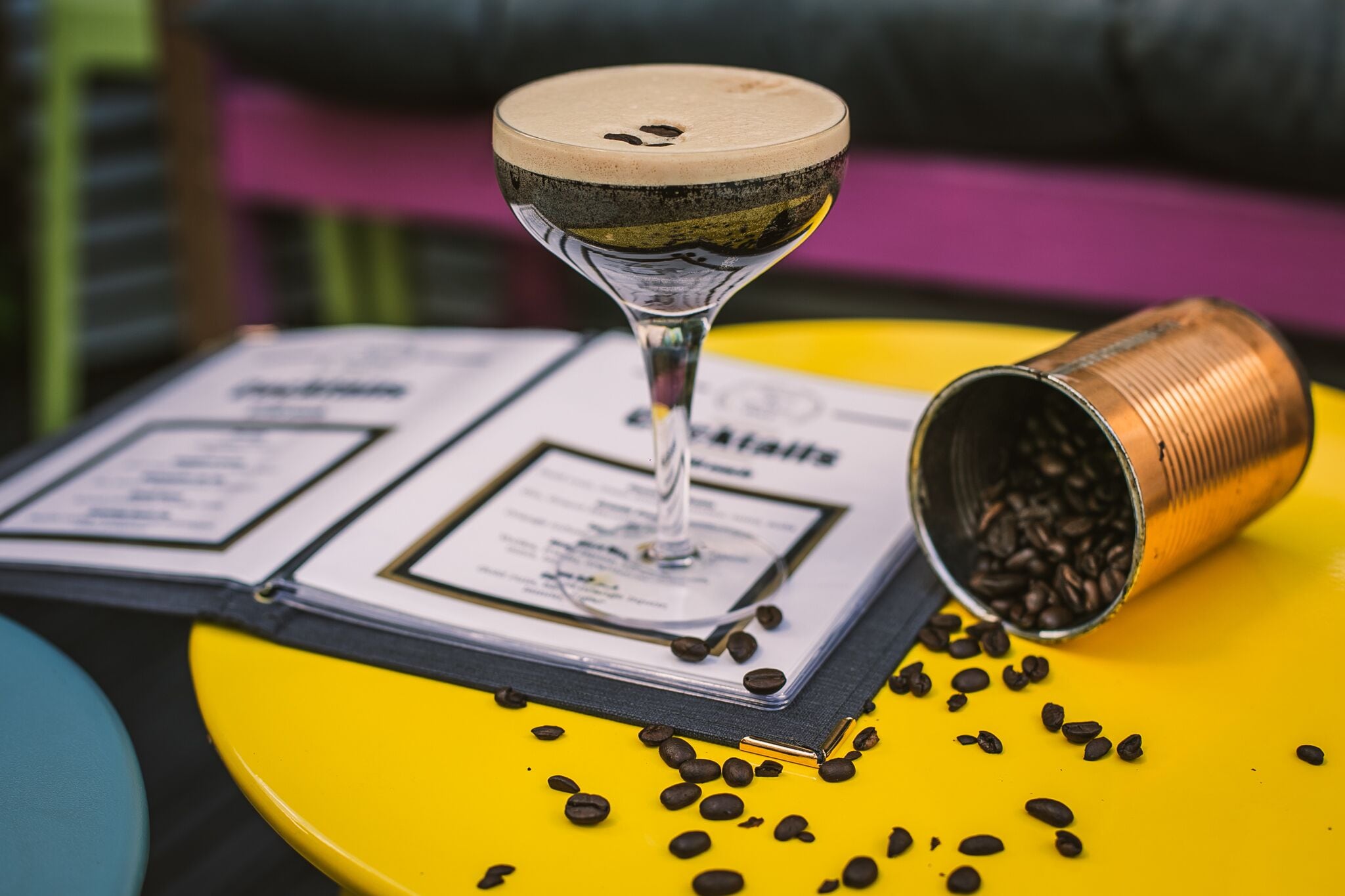 A menu with a drink in a glass, a can of coffee beans, and a yellow table.