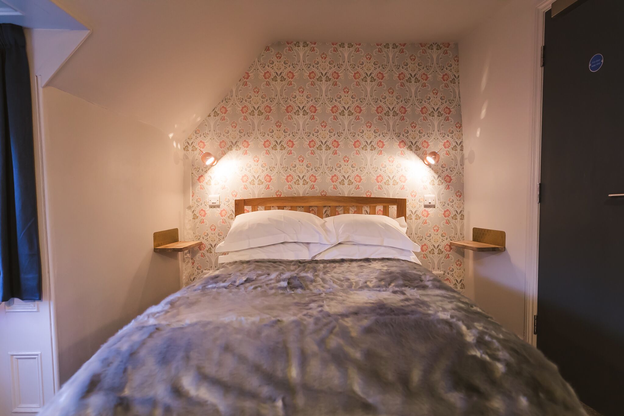 A bedroom with a bed, floral wallpaper, and bedside lamps.