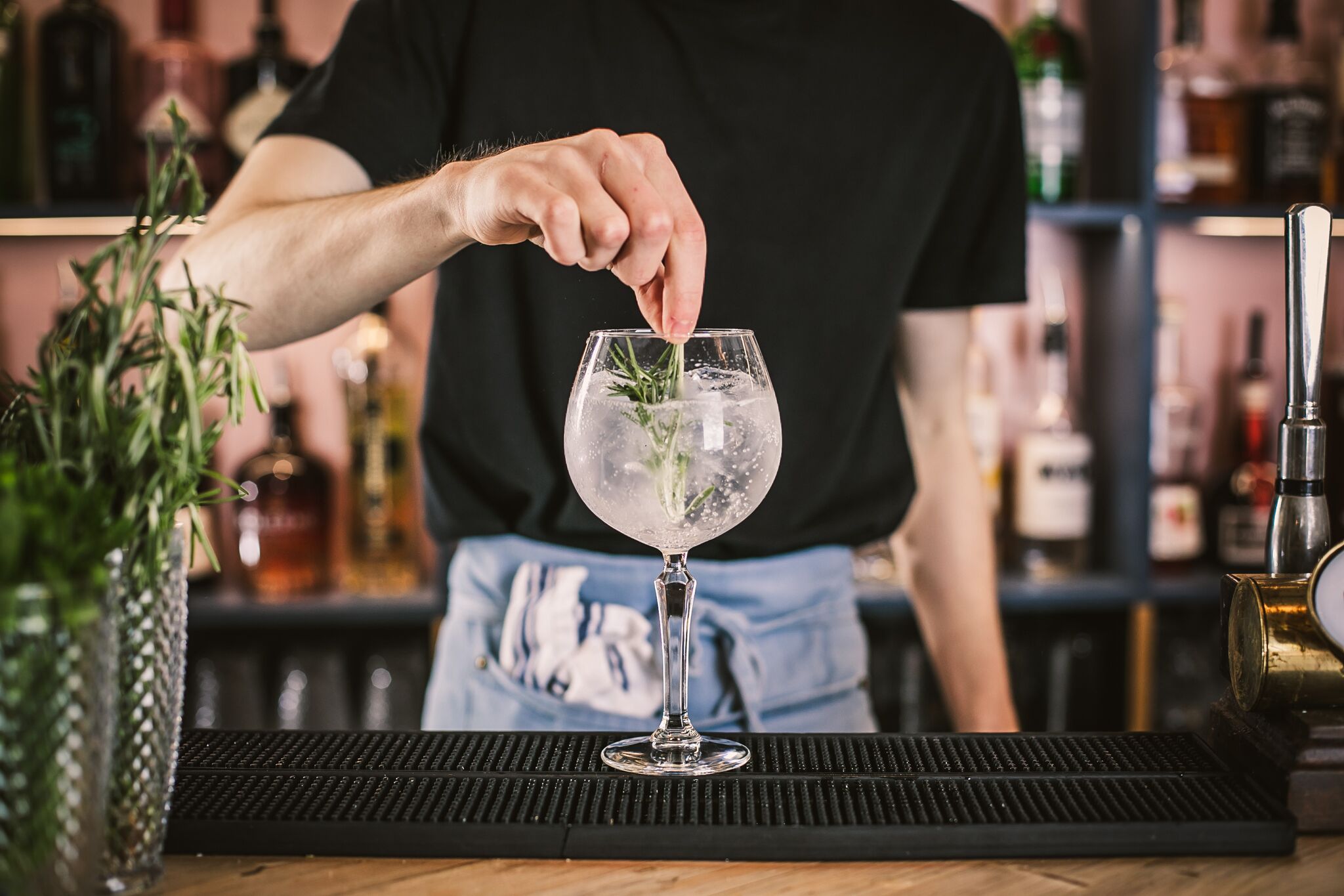 Een barman maakt een drankje met een takje rozemarijn in een glas.