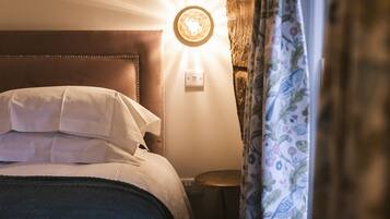 A bed with white linens, a round wall light, and a small round table beside it.