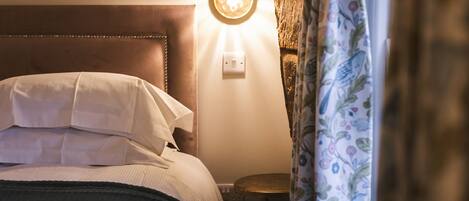 A bed with white linens, a round wall light, and a small round table beside it.