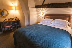 Un dormitorio con una cama grande, una silla de madera, un escritorio con una lámpara y un espejo montado en la pared.