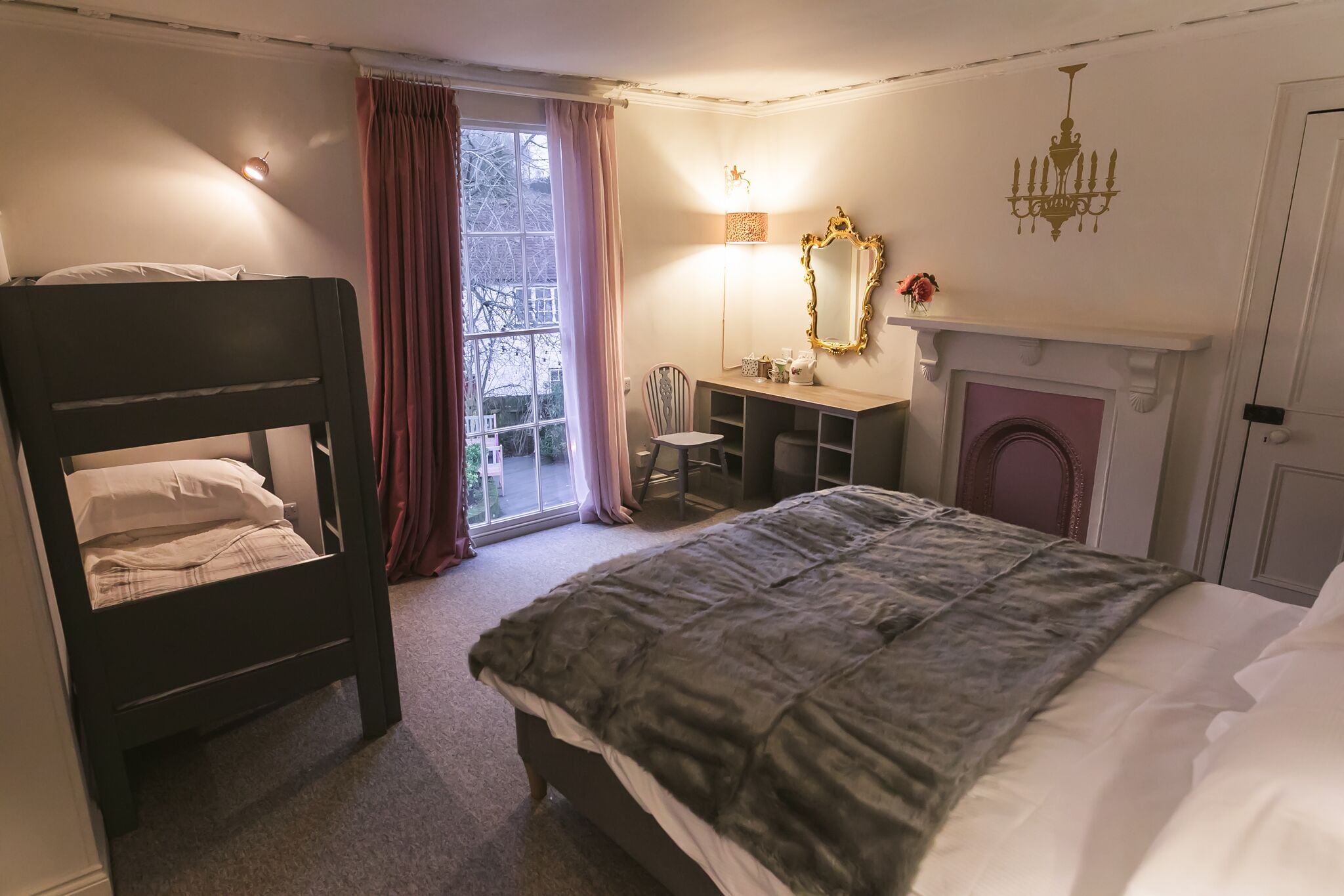 A bedroom with a bunk bed, a desk, a chair, a fireplace, and a large window with curtains.