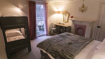 A bedroom with a bunk bed, a desk, a chair, a fireplace, and a large window with curtains.