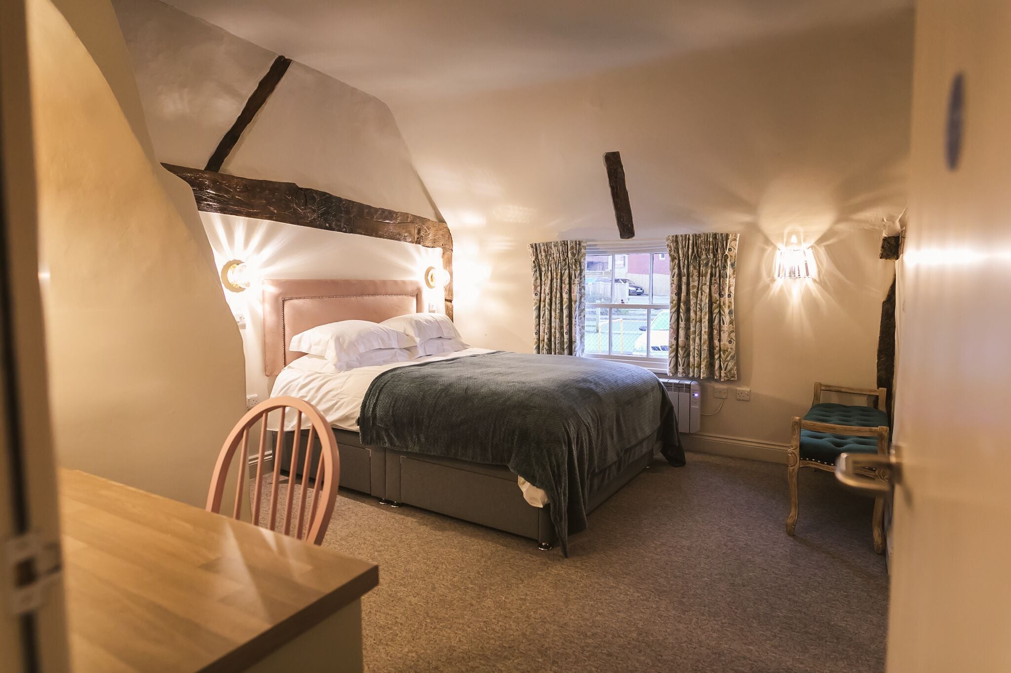 A bedroom with a bed, a chair, a table, and a window with curtains.