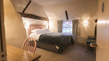 A bedroom with a bed, a chair, a table, and a window with curtains.