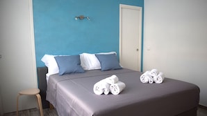Una cama bien hecha con una colcha gris, dos almohadas y toallas enrolladas sobre la cama.