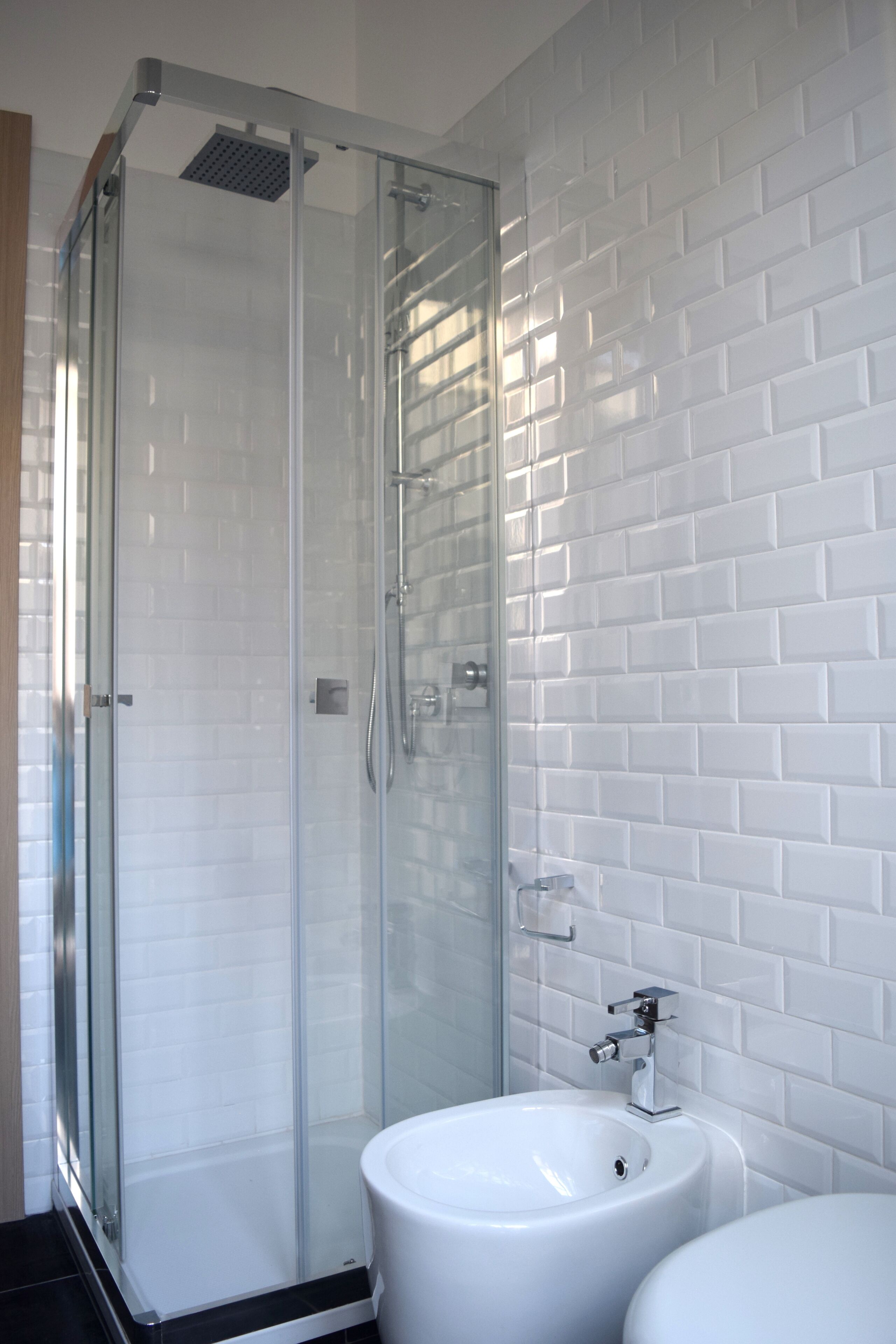 Une salle de bain moderne avec une douche à parois de verre, des murs recouverts de carreaux blancs et un lavabo blanc.