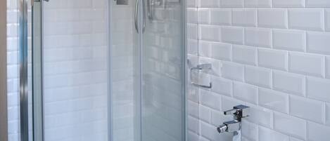 Une salle de bain moderne avec une douche à parois de verre, des murs recouverts de carreaux blancs et un lavabo blanc.