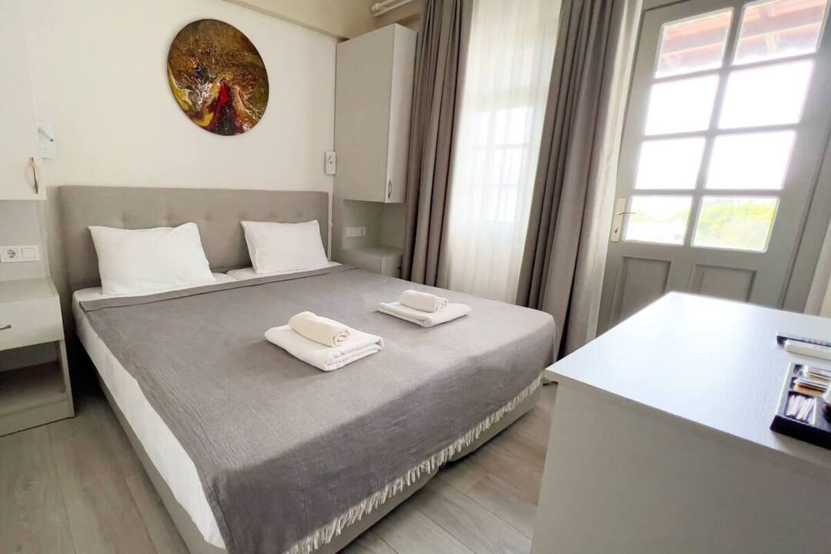 Ein modernes Hotelzimmer mit Bett, Nachttischen, einem Schreibtisch und einem Fenster mit Vorhängen.