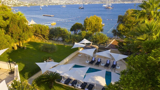 A pool area with lounge chairs and umbrellas, overlooking a marina with boats. - Farrys Boutique Hotel & Beach Club (Bodrum)
