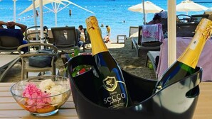 A beachside table with a black bucket containing two champagne bottles, a bowl of flowers, and a view of the sea with boats. - Farrys Boutique Hotel & Beach Club (Bodrum)