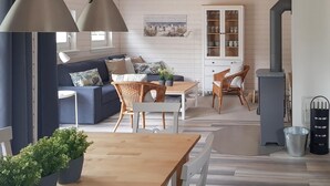 Ein modernes Wohnzimmer mit einer Couch, einem Esstisch und Stühlen. Es gibt ein Sideboard mit Glastüren und einen Blumentopf auf dem Tisch.