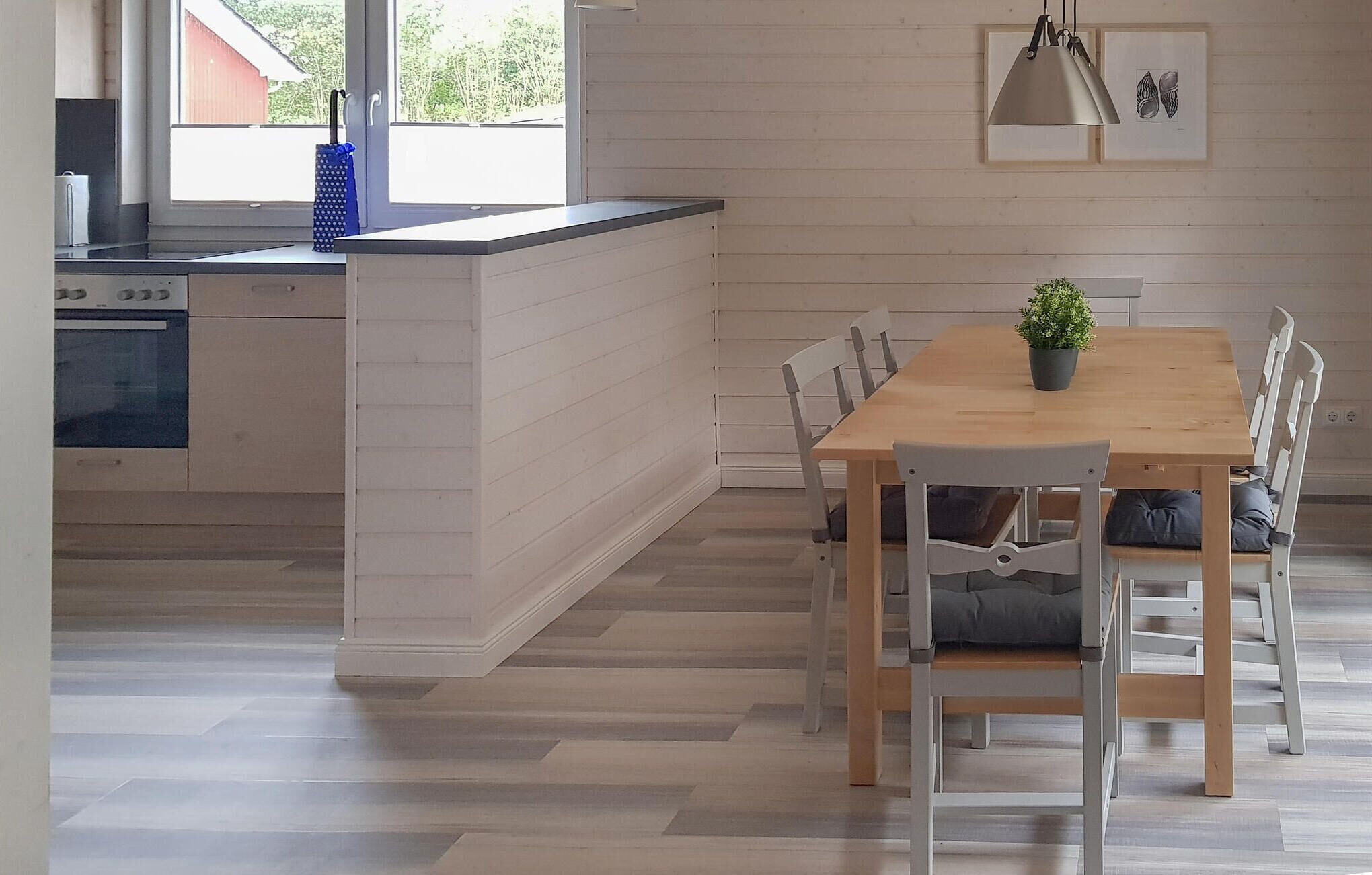 A modern kitchen with a wooden island, a dining area with a wooden table and chairs, and a view of the outdoors through large windows.