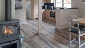 Eine moderne Küche mit Kaminofen, einem Essbereich mit Tisch und Stühlen sowie Blick auf einen Leuchtturm durch ein Fenster.