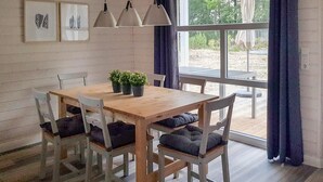 Ein Essbereich mit Holztisch und Stühlen, Topfpflanzen, Pendelleuchten und Blick durch große Fenster.