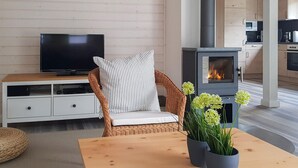 Ein modernes Wohnzimmer mit Fernseher, einem Korbsessel mit gestreiften Kissen, einem kleinen Tisch mit Blumenvase und einem Holzofen.