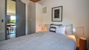 A bedroom with a checkered bedspread, a framed abstract art piece above the bed, and a wooden floor.