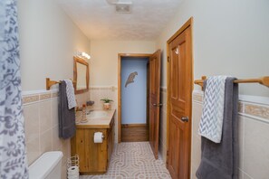 A bathroom with a wooden vanity, a mirror with lights, a towel rack, and a door leading to another room. - Beachfront apartment with excellent snorkeling (Roatan)