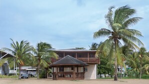 A two-story building with a balcony, surrounded by palm trees and a sandy ground. - Beachfront apartment with excellent snorkeling (Roatan)