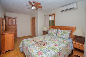 Un dormitorio con una cama de madera, dos mesitas de noche con lámparas, un ventilador de techo y un equipo de aire acondicionado.