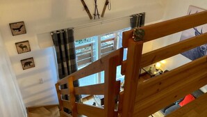 A wooden staircase with a view of a room below, including a window with curtains and a bed with a red blanket. - Duplex 2-bedroom in Brides-les-Bains center, balcony, elevator, pets allowed (Brides-les-Bains)