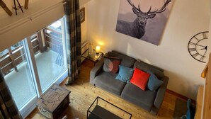 A living room with a grey sofa, a clock, and a deer painting. - Duplex 2-bedroom in Brides-les-Bains center, balcony, elevator, pets allowed (Brides-les-Bains)