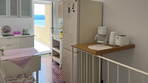 Eine kompakte Küche mit Kühlschrank, Kaffeemaschine und Toaster. Ein kleiner Esstisch mit einem Stuhl ist zu sehen.