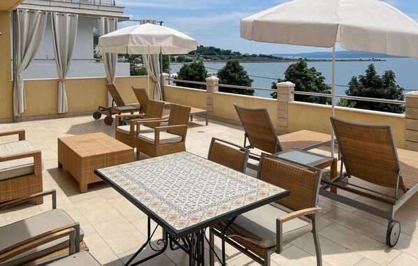 An outdoor terrace with wicker furniture, a tiled table, and white umbrellas.