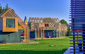 Un edificio moderno con una fachada de celosía de madera singular, una pequeña torre y un área verde con una bicicleta.