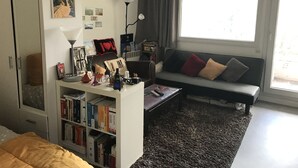 A living room with a sofa, a bookshelf, and a window with curtains.