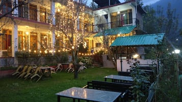 Relax in our serene outdoor seating area surrounded by lush gardens and a charming building with traditional architecture.