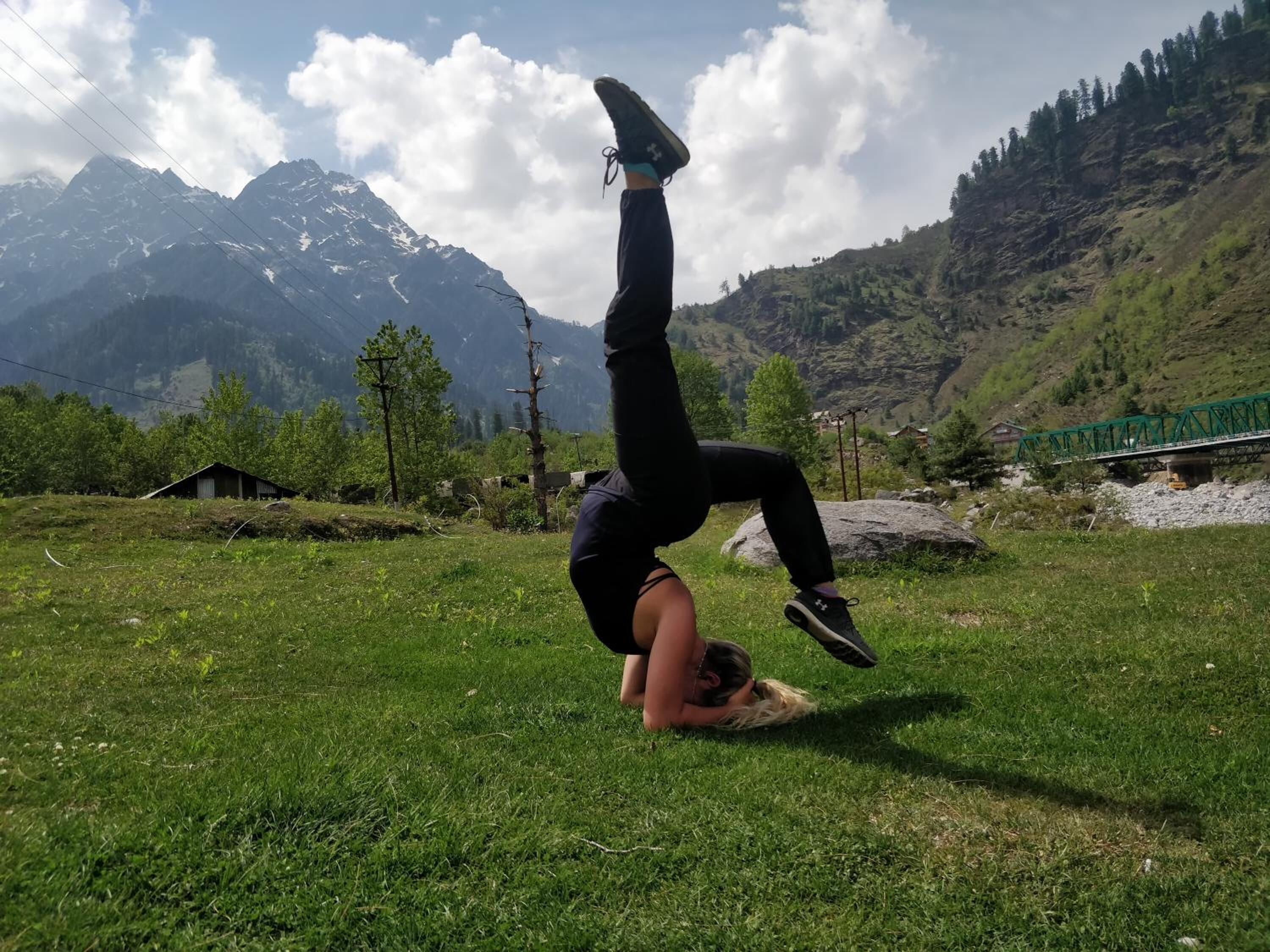 Una persona realizando un movimiento acrobático en un campo cubierto de hierba, con montañas al fondo.