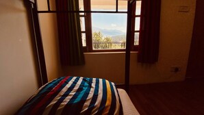 Een stapelbed met een gestreepte spreidekbed in een kamer met een raam dat uitkijkt op een balkon en bergen.