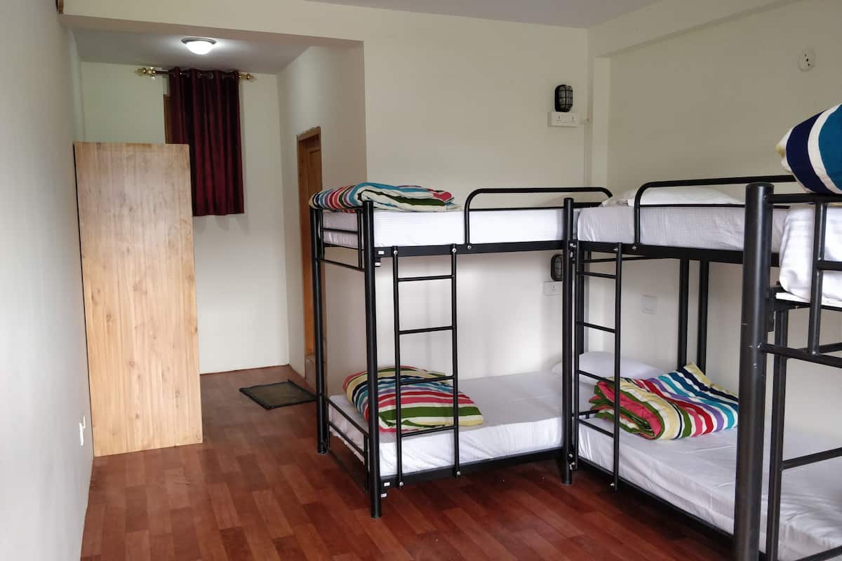 Habitación con literas, suelo de madera, una puerta y un enchufe en la pared.