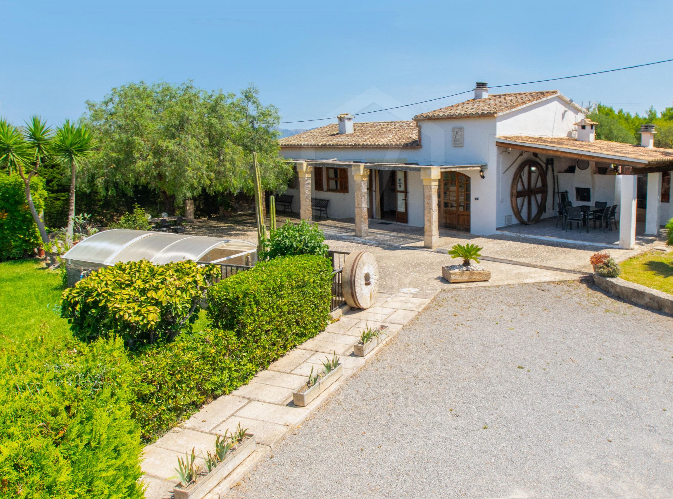 Una villa con patio, mobiliario exterior y una noria grande.