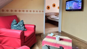 A cozy room with a red sofa, a bed with sunflowers, a TV, and a small table with a remote. - Cozy 2 pers. Vacation apartment "Sunflower" (Irmenach)