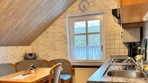 A cozy kitchen with a dining area, featuring a clock, a window with a view, and a radiator. - Cozy 2 pers. Vacation apartment "Sunflower" (Irmenach)