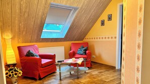 A cozy room with a sloped ceiling, two red armchairs, a glass coffee table, and a skylight. - Cozy 2 pers. Vacation apartment "Sunflower" (Irmenach)