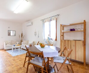 Un coin repas comprenant une table ronde, des chaises, un meuble en bois et une fenêtre avec des rideaux.
