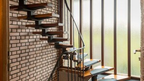 A modern staircase with wooden steps and metal railings, leading to a room with a brick wall and a large window.