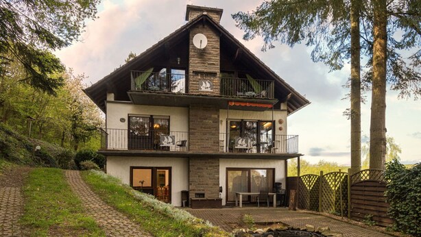 Une maison à deux étages avec un balcon, une cheminée et une allée pavée.