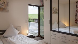 Une chambre à coucher comprenant un lit, une table de chevet, une lampe de chevet, une armoire et une porte-fenêtre coulissante donnant sur un espace extérieur.