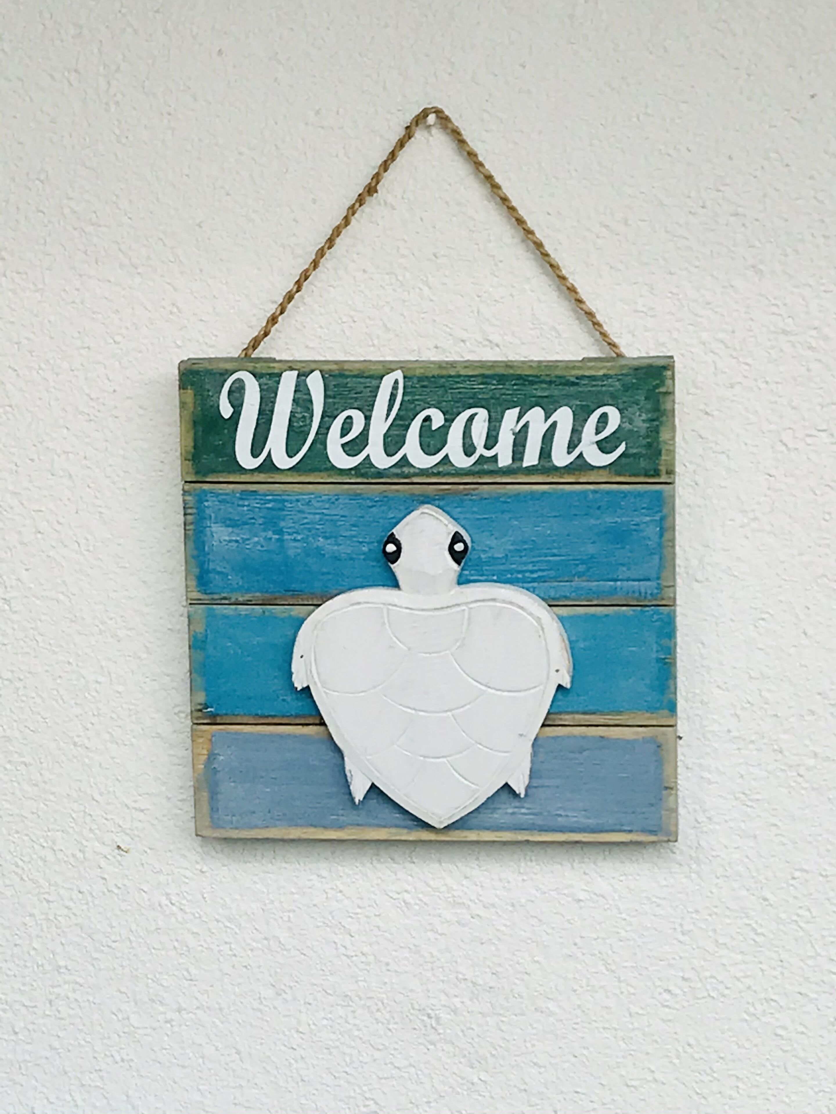 Une enseigne d’accueil ornée d’un motif de tortue et portant le mot « Bienvenue », le tout sur un fond en bois.