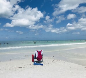 Ein Strand mit einem roten Rucksack im Sand, einem klaren Himmel und Menschen im Wasser.