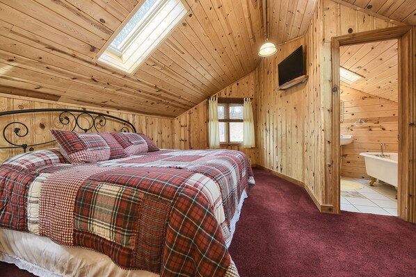 Een slaapkamer in een houten hutje, met een bed, een televisie en een badkamer die door een open deur zichtbaar is.