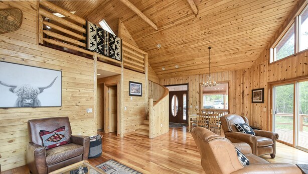 Ein geräumiger Holzraum mit hoher Decke, Ledersofas, einem Glastisch und einem Essbereich mit Tageslicht.