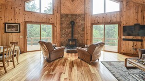 Ein Holzblockhaus-Interieur mit Kamin aus Stein, Ledersesseln und einem Fernseher.