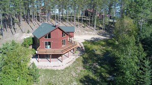 Eine Hütte mit einer Veranda, umgeben von dichtem Wald und wolkenlosem Himmel.
