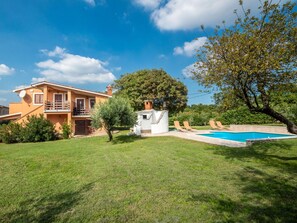 Une maison à deux étages avec une piscine, une cuisine extérieure couverte et un grand arbre dans le jardin.